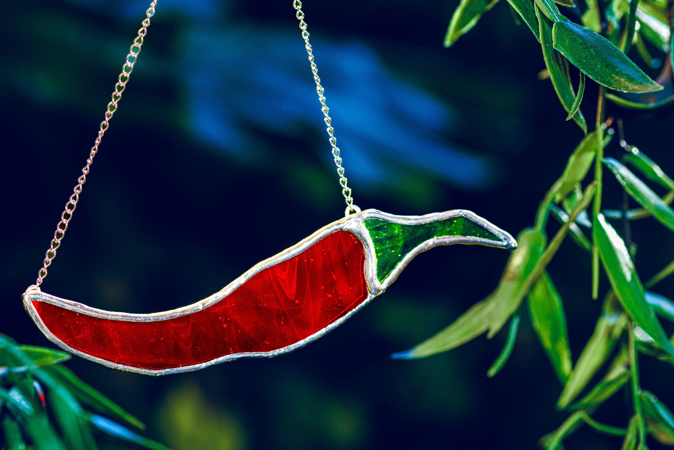Stained glass red chili pepper hanging among green leaves