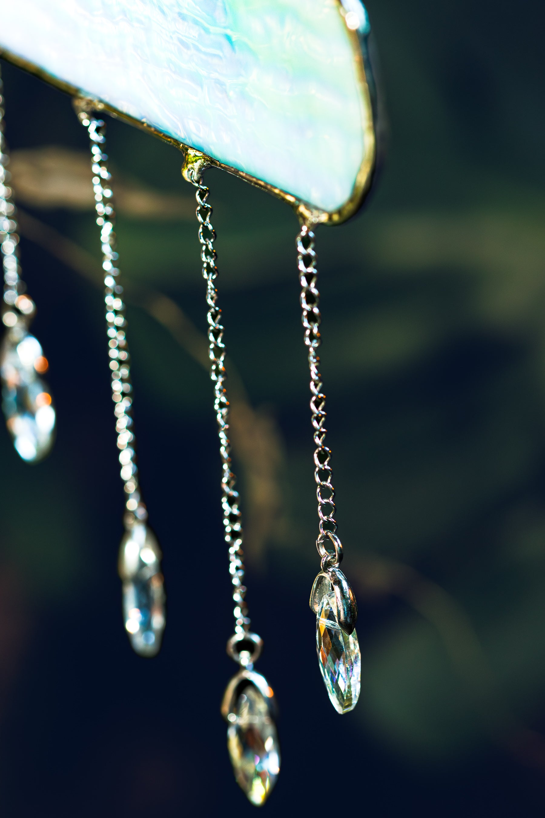 Silver chain earrings with clear crystal pendants against a blurred natural background